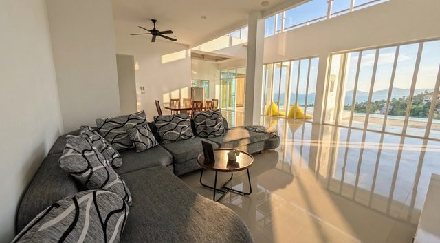 Bright living room with a large grey sofa, panoramic glazing and pool access
